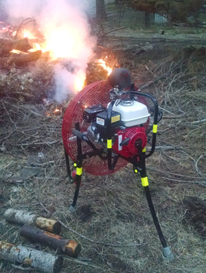 All-Terrain Ventry Fan Model 24GX160 with optional Solid Rubber Wheels & Skids and Top Light LED shown assisting the burn of a brush pile. The three independently adjustable legs are extended at different lengths in order to aim the fan directly at the heart of the fire and to allow the fan to be lifted above the ground debris so it is not sucked up in the the fan.