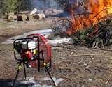 All-Terrain Ventry Fan Model 24GX160 with a 24-inch prop and optional Medium Flat-Free Wheels shown assisting the burn of a brush pile. The three independently adjustable legs are extended at different lengths, allowing the fan to be placed in the mud and straddling ground debris.